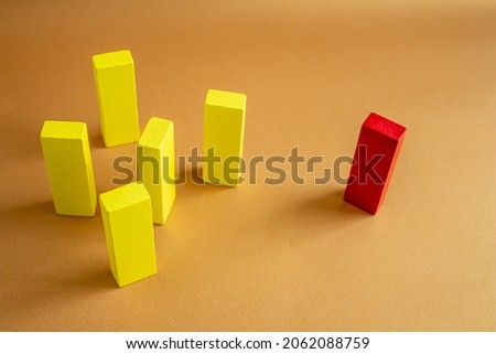 A single red block standing away from a group of yellow wooden blocks. Concept of individuality, discrimination, exclusion, loneliness.