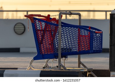 A Single Red And Blue Shopping Cart On A Empty Parking Spot With Sunset On The Background