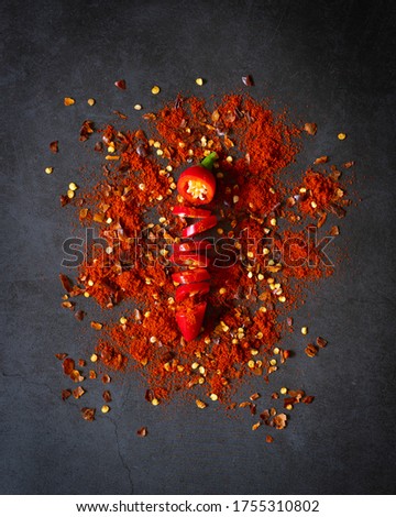 Single red chilli sliced into small pieces laid out vertically  on distressed kitchen work surface with chilli seeds and powder sprinkled around chilli - portrait aspect