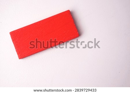A single red rectangular wooden block placed diagonally on a clean white background. Minimalist stock photo representing priority, alert, single step, focal point, and abstract design with copy space.