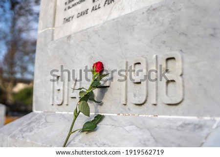 Single red rose placed against marble Great War soldier memorial on Sunday 11th November remembrance day for those who lost their lives 1914 1918