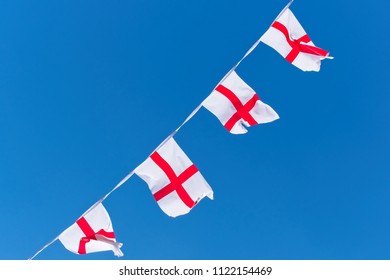 Single Row Of England Flags / Bunting Flying Against Blue Sky.