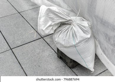 Single Sandbag, White Plastic Bag Filled With Sand Used As A Weight To Hold Construction Steady.