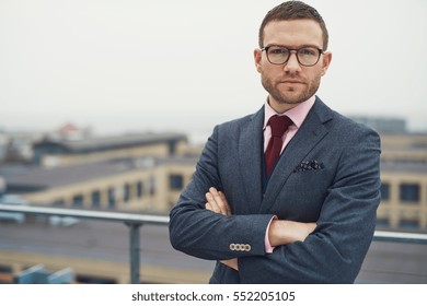 Single serious handsome bearded young businessman in eyeglasses, red necktie leaning against railing outdoors - Powered by Shutterstock