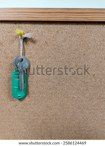 A single silver key with green keyring hanging on a noticeboard
