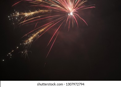 single skyrocket exploding on night sky in red and golden sparkling colors
