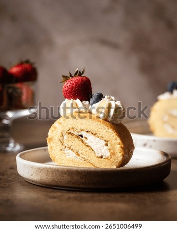 Single slice of berry roll cake on white ceramic plate with strawberry topping.