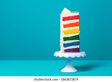 Single slice of birthday cake on a white cakestand minimalist on a blue background. Homemade cake with multicolored layers and buttercream - Shutterstock ID 1863873874