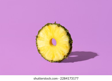Single slice of pineapple in bright light minimalist on a purple table. Slice of a pineapple fruit isolated on a vibrant background