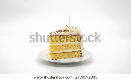 A single slice of yellow cake with white frosting and colorful sprinkles sits on a white plate, topped with a single unlit white candle.
