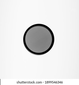 A single small camera lens filter photographed in black and white on a light board