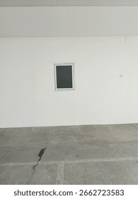 A single small square window on a plain white wall with concrete ground. Urban minimalism, simple architecture background.