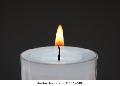 Single Small White Candle Burning. Close Up Studio Shot, Isolated On Dark Background.