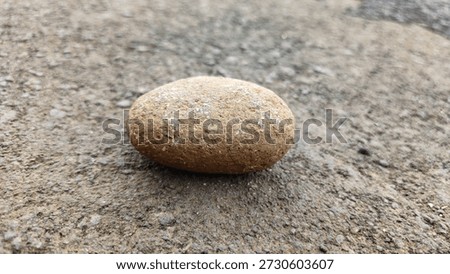 Single smooth river stone on rough asphalt background. Minimalist pebble for zen meditation, nature concept, construction material, and wellness spa decoration.