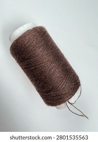 Single spool of dark brown sewing thread isolated on a white background.