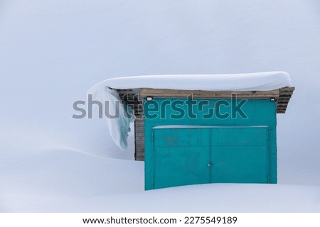 Single standing garage covered in deep snow in winter season. Snowdrift on the roof above garage. Green garage against the background of white snowdrifts. Gate access closed until spring or clearing