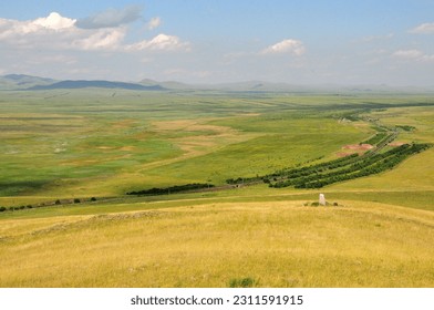 A single stone menhir on the slope of a high hill with yellowed grass overlooking the boundless summer steppe. Mount Uitag, Khakassia, Siberia, Russia. - Shutterstock ID 2311591915