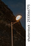 A single streetlamp glowing warmly against a rocky hillside during the evening