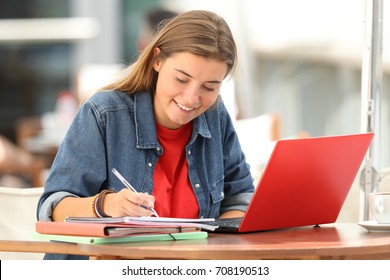 Single Student E-learning On Line With A Laptop And Taking Notes Sitting In A Bar