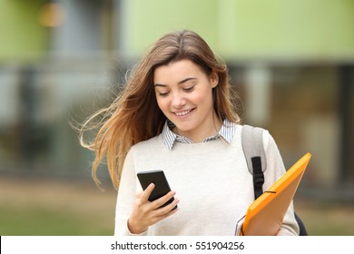 Single Student Walking And Reading Mobile Phone Messages With A University Building In The Background