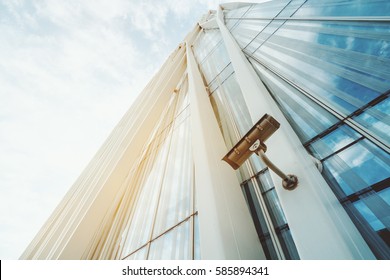 Single Surveillance Camera On Facade Of Contemporary Business Skyscraper On Sunny Summer Day, Security Camera On Metal Beam Of Modern Office Building With Copy Space For Your Logo Or Message Text