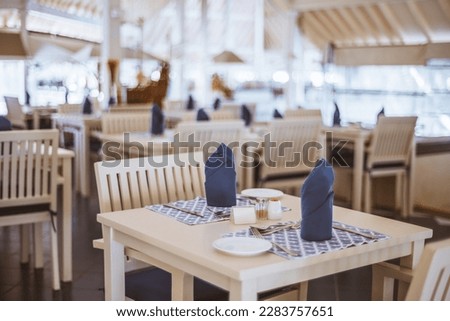 A single table with blue decoratively folded napkins, silverware, and a blue sous plat. Selective focus draws attention to the table setting, highlighting its elegance and attention to detail