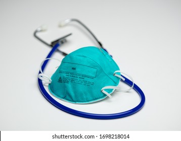 An Single Teal N95 Respirator Mask On Top Of A Blue Medical Stethoscope. Isolated On A White Background.