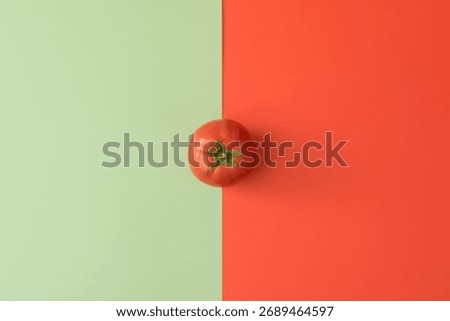 Single tomato on split green and red background. Minimal color contrast. Creative complementary flat lay food concept.