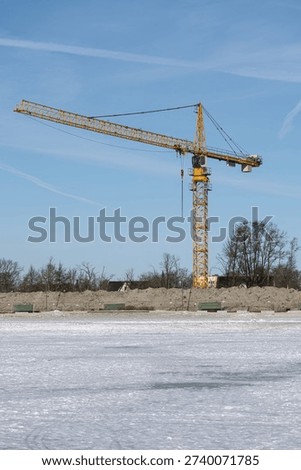 Single tower crane at winter construction site beside frozen water, urban development and infrastructure growth concept