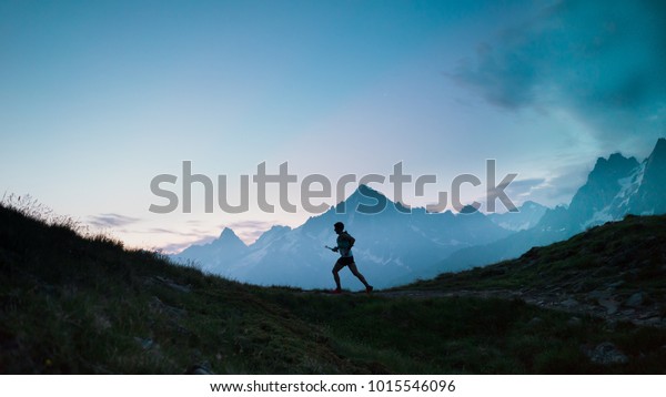 A single trail runner, silhouetted against the sky\
at sunrise while running in the mountains of the Alps along a steep\
trail