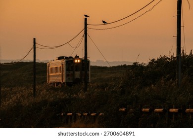 A single train car running through the landscape at sunset, with an orange sky and dramatic silhouette, creates a serene and picturesque evening scene.