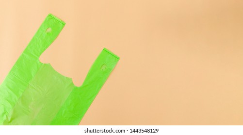 Single Use, Green Plastic Bag From Supermarket Cut Off, Flat Lay On Light Brown Background With Copy Space For Recycling And Environmental Concept.