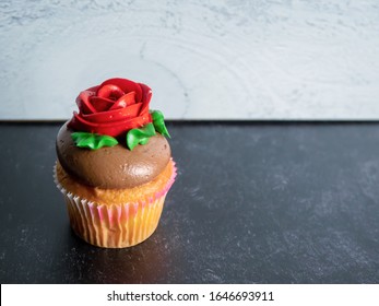 Single Vanilla Cupcake With Chocolate Frosting Decorated With A Red Rose And Green Leaves Against A Black Slate And Gray Shiplap Background, Perfect For A Birthday, Mother’s Day, Or Valentine’s Day!