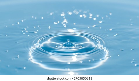 A single water drop is captured mid-fall, creating concentric ripples on a smooth, bright blue liquid surface. Numerous small, bright bokeh lights are scattered across the surface.