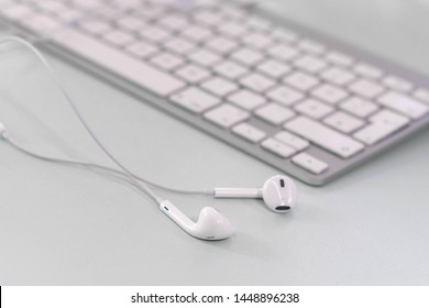 Single White Ear Pods Lying Next To A Clean Keyboard