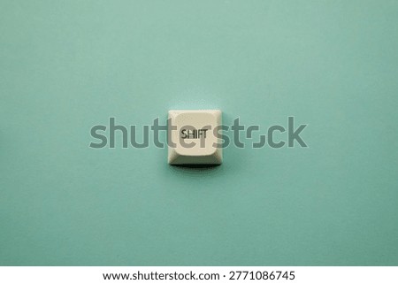 A single white keyboard keycap labeled SHIFT is centered on a textured mint green surface. The minimalist composition serves as a metaphor for paradigm shifts and systemic transformation.