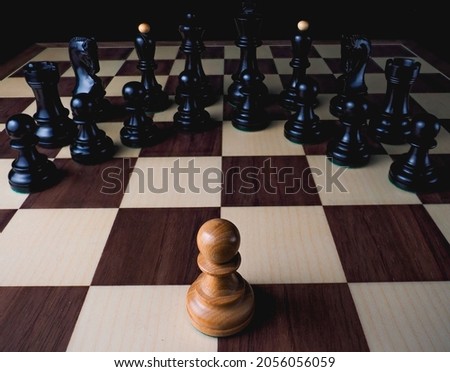 A single white pawn faces all the black pieces on a chess board.