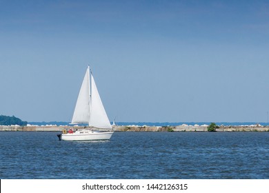 A single white sailboat crosses the harbor inside the breakwall at Cleveland, Ohio on Lake Erie