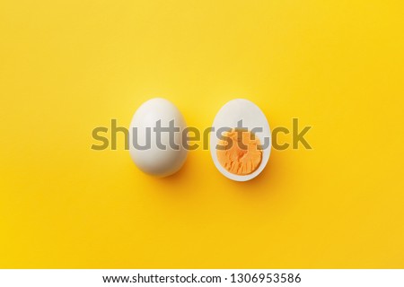 Single whole white egg and halved boiled egg with yolk on a yellow background. Top view