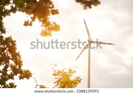 A single wind turbine produces electric power from renewable wind energy in a rural landscape, creating a silhouette against the sunny sky. wind turbine generates electric power in a sustainable way.