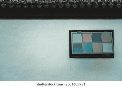 A single window with a dark frame and patterned glass panes, set into a white plastered wall. - Powered by Shutterstock