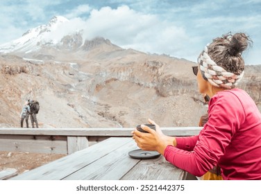 Single woman alone sit drink beverage watch happy tourist couple hikers in mountains viewpoint cafe.Kazbek mountain peak panorama in Kazbegi national park. Travel explore Georgia destination in autumn - Powered by Shutterstock