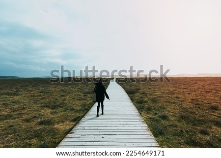 Single woman walking an endless wooden path to the dunes