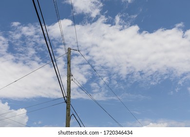 Single Wood Power Pole With Transmission Wires Radiating Out In Three Directions Against A Blue Sky With Clouds, Creative Copy Space, Horizontal Aspect