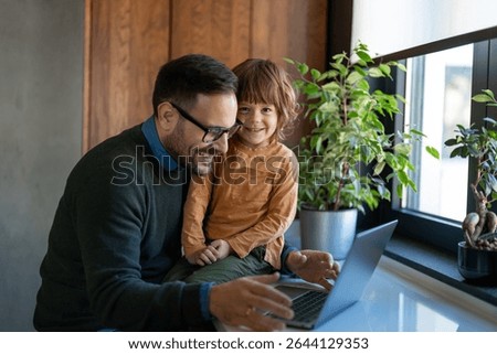 Single working dad spend time with small kid, sit together work on laptop. Happy family, parenthood
