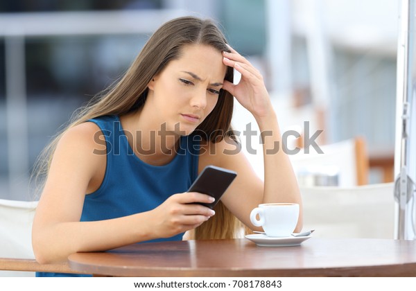 Single worried woman\
watching a mobile phone and waiting for a call or message sitting\
in a coffee shop