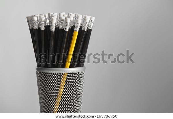 Single yellow\
pencil in pot of black\
pencils.