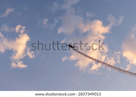 A single-engine aerobatic plane leaves a dramatic smoke trail across sunset clouds during Aerobatic Air Show in Chilliwack, BC Canada.