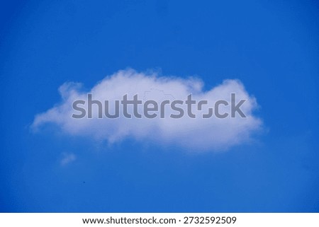 A singular fluffy cloud floating in the vast expanse of a clear blue sky. The cloud is gently illuminated, creating a soft and dreamy atmosphere