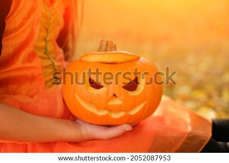A sinister Halloween pumpkin in the hands of a girl in an orange carnival dress. jack o' lantern. Traditions for the holiday. copy space  Foto stock © 